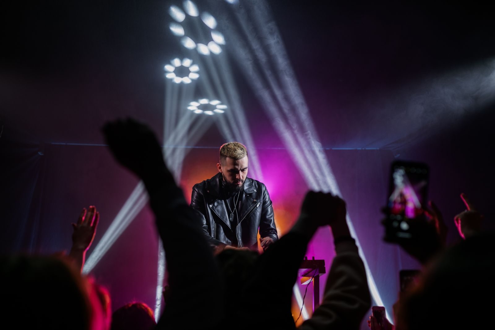 Headline artist performing on stage as the crowd films under purple lights