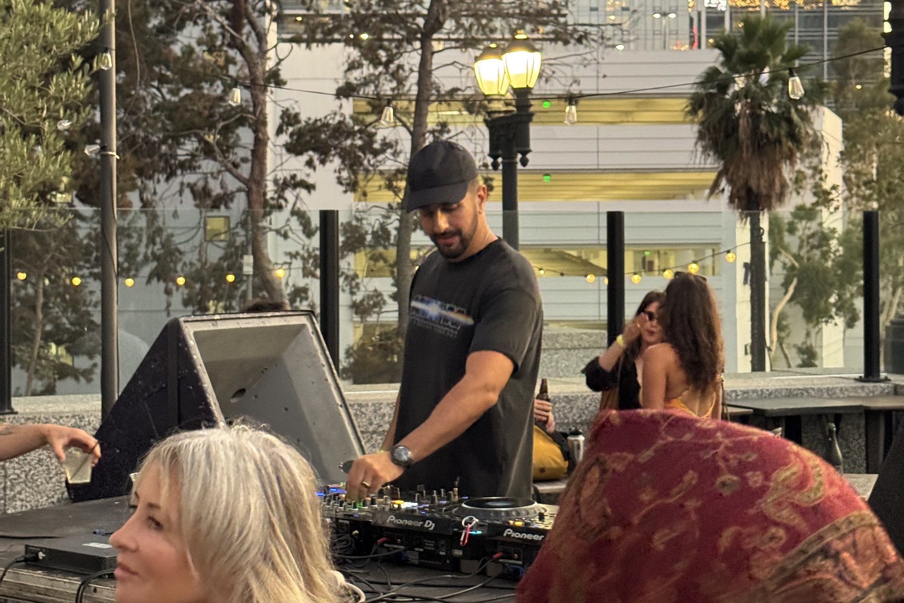 DJ performing on an outdoor Los Angeles rooftop at dusk with guests gathered around the booth